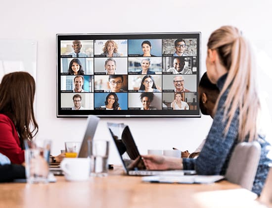 Personale in una sala riunioni che guarda un display con una videoconferenza in corso
